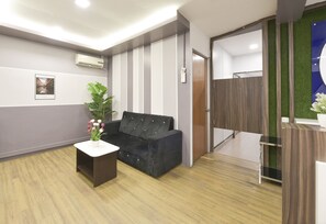A modern reception area with a black sofa, a small table with a potted plant, and a wooden floor. - Hotel O Gest Inn (Kota Tinggi)