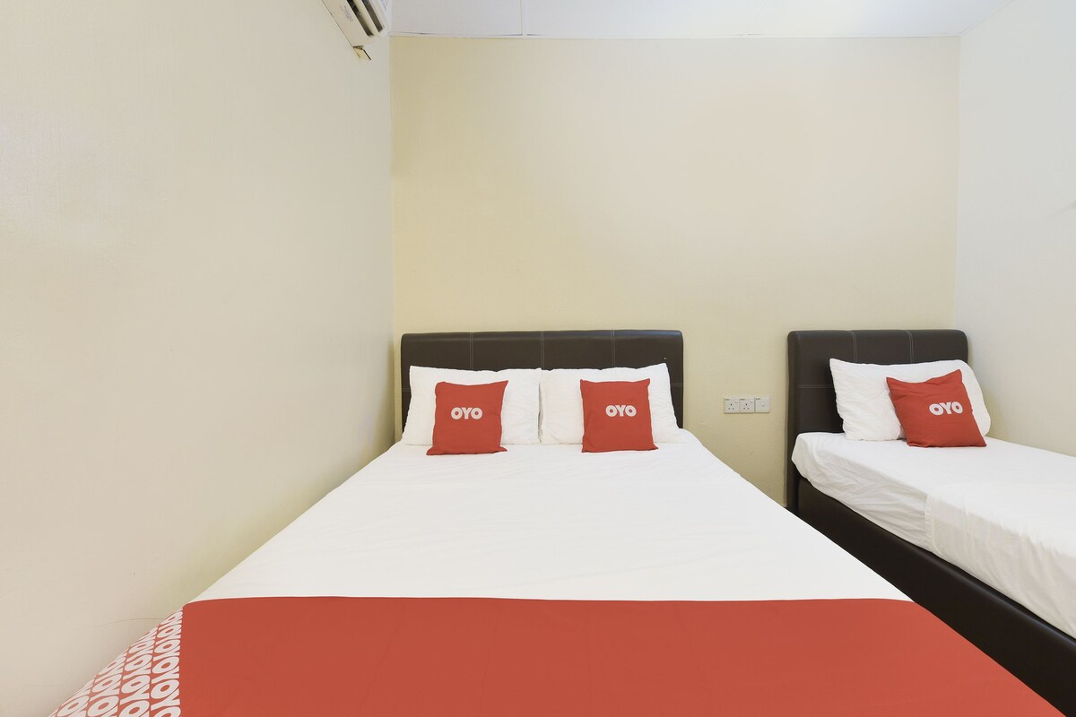 A hotel room with two beds, each with white bedding and red pillows with the logo 'OYO'.