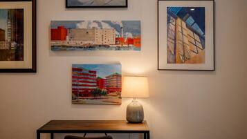 A room with a table, a lamp, and four framed paintings on the wall.