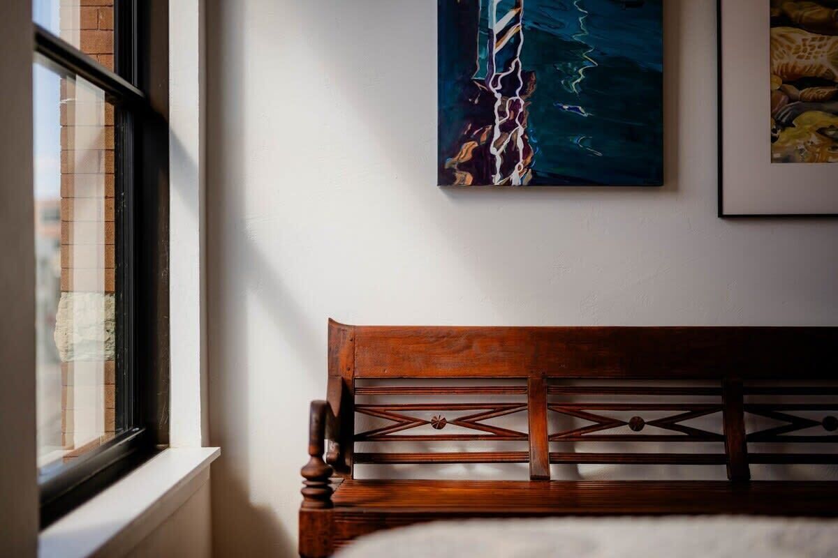 Una stanza con una testiera in legno, un quadro astratto incorniciato e una finestra che dà su un muro di mattoni.
