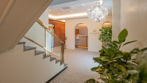A hotel lobby with a staircase, a reception desk, and a hanging chandelier. - H Avenue Munhyeon (Busan)