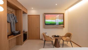 A modern hotel room with a wooden wardrobe, a TV mounted on the wall, two chairs, and a small table.