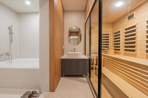 A modern bathroom with a bathtub, a sink, and a wooden sauna area. - H Avenue Munhyeon (Busan)