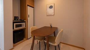 A compact room with a wooden cabinet, a microwave, a small refrigerator, and a dining table with two chairs. - H Avenue Munhyeon (Busan)