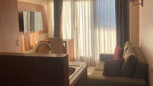 A hotel room with a kitchenette, a sofa, a TV mounted on the wall, and a window with curtains. - Mb Residence Osmanbey (Istanbul)