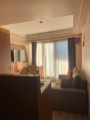 A hotel room with a kitchenette, a sofa, a TV mounted on the wall, and a window with curtains. - Mb Residence Osmanbey (Istanbul)