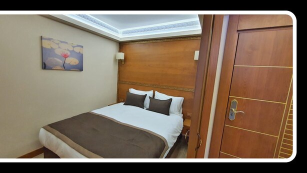A hotel room with a bed, a painting on the wall, and a wooden door.
