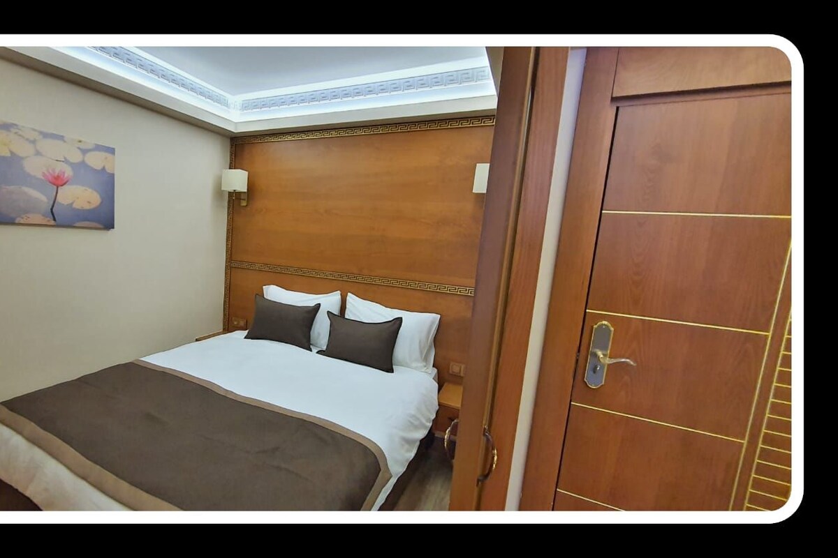 A hotel room with a bed, a painting on the wall, and a wooden door.