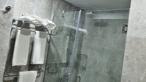 A modern bathroom with a glass-enclosed shower, marble tiles, and a towel rack with multiple towels.