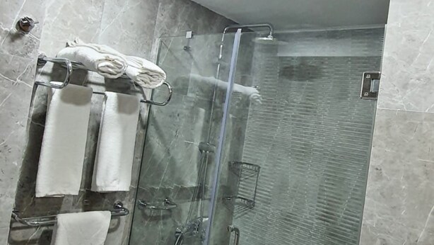 A modern bathroom with a glass-enclosed shower, marble tiles, and a towel rack with multiple towels. - Mb Residence Osmanbey (Istanbul)