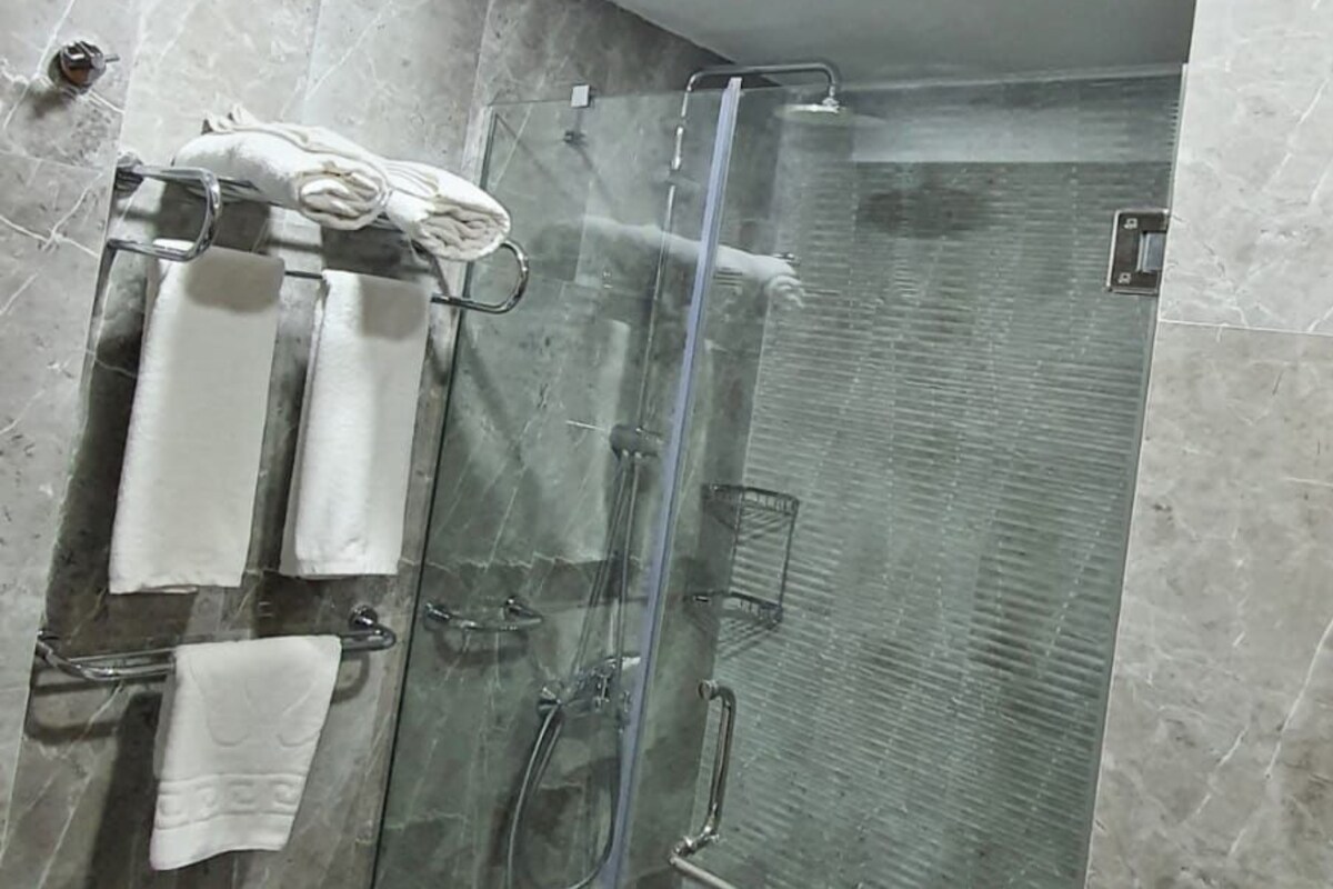 A modern bathroom with a glass-enclosed shower, marble tiles, and a towel rack with multiple towels.