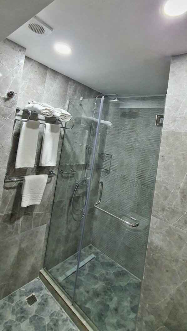 A modern bathroom with a glass-enclosed shower, marble tiles, and a towel rack with multiple towels.