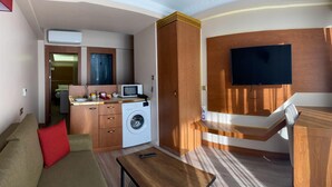 A compact living space with a sofa, a washing machine, a small kitchenette, and a TV mounted on the wall. - Mb Residence Osmanbey (Istanbul)