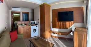 A compact living space with a sofa, a washing machine, a small kitchenette, and a TV mounted on the wall. - Mb Residence Osmanbey (Istanbul)