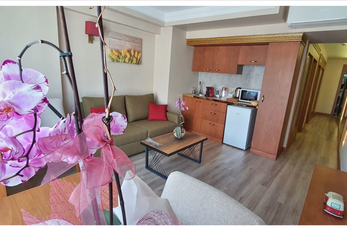 A modern living room with a sofa, a coffee table, and a kitchen area with cabinets and appliances.