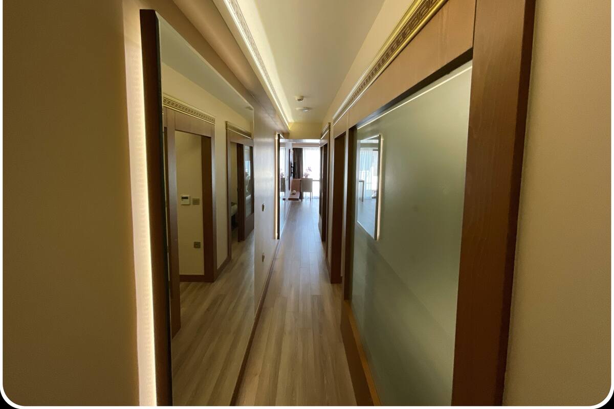 A hotel corridor with wooden floors, doors, and a light-colored wall.