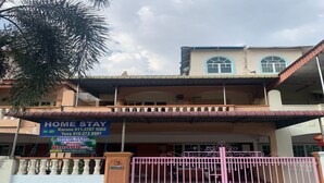 Un edificio de dos plantas con un balcón, una entrada porticada y un letrero que anuncia alojamientos en casas particulares.