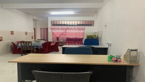 Un comedor con una mesa larga, sillas y una pequeña área de cocina con refrigerador y fregadero.