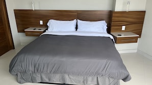 Een moderne slaapkamer met een groot bed, een houten hoofdbord, twee nachtkastjes en een bijzettafeltje met een afstandsbediening.