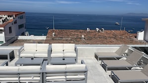 Een terras op het dak met witte lounge stoelen en uitzicht op zee.