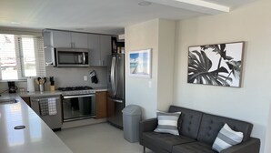 Een moderne keuken met een centraal eiland, roestvrijstalen apparatuur en een grijze bank met gestreepte kussens.