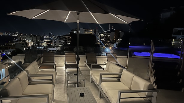 Een terras met een grote parasol, meerdere stoelen en een zwembad op de achtergrond.