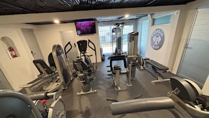 Een sportschool met cardioapparaten, gewichthefapparatuur en een televisiescherm waarop een trainingsvideo wordt afgespeeld.
