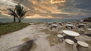 A beachside area with concrete tables and benches, a palm tree, and a view of the sea under a cloudy sky. - Hotel O Teratak Samuderakita, Chalet & Guesthouse (Kuala Terengganu)