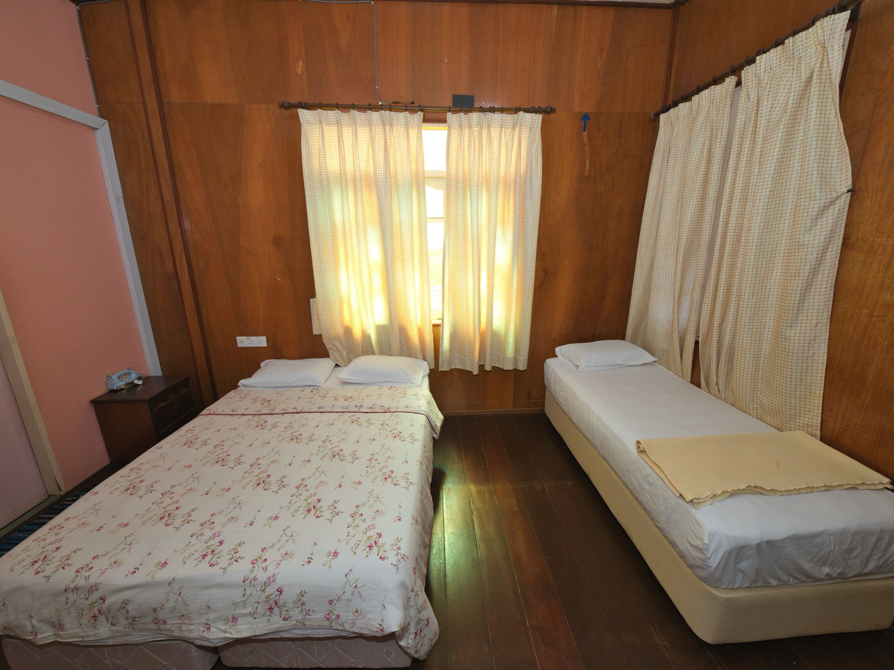 Une chambre avec deux lits, des murs en bois et une fenêtre avec des rideaux.