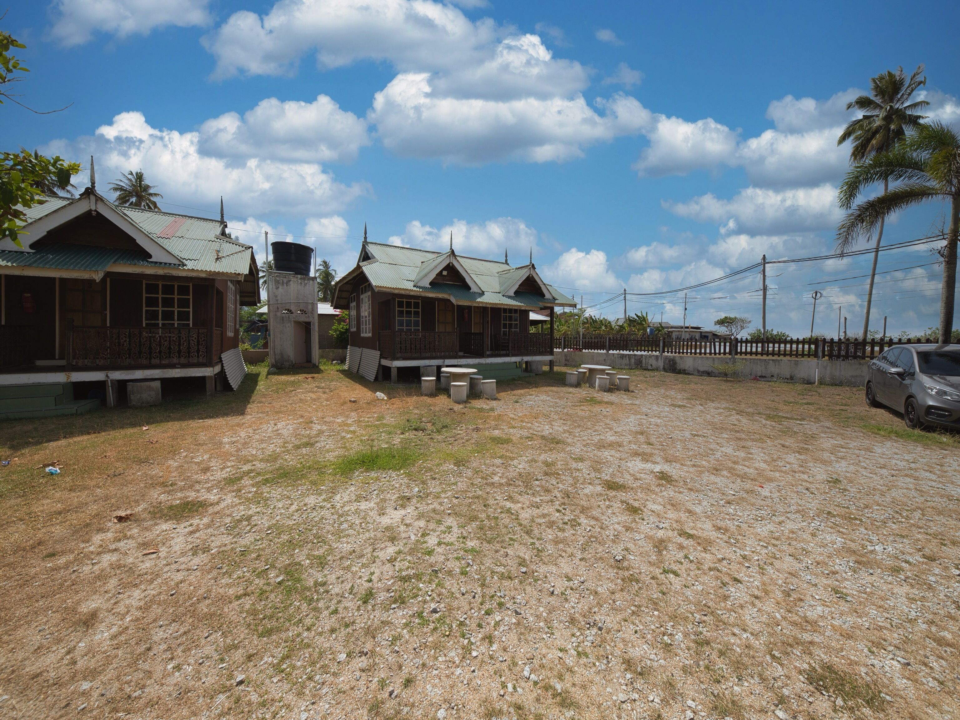 A row of simple, single-story cabins with metal roofs, surrounded by a grassy area and a fence.