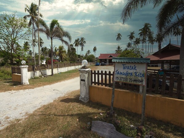 A gated entrance with a sign for Teratak Samudera Kita, a dirt road, and palm trees. - Hotel O Teratak Samuderakita, Chalet & Guesthouse (Kuala Terengganu)