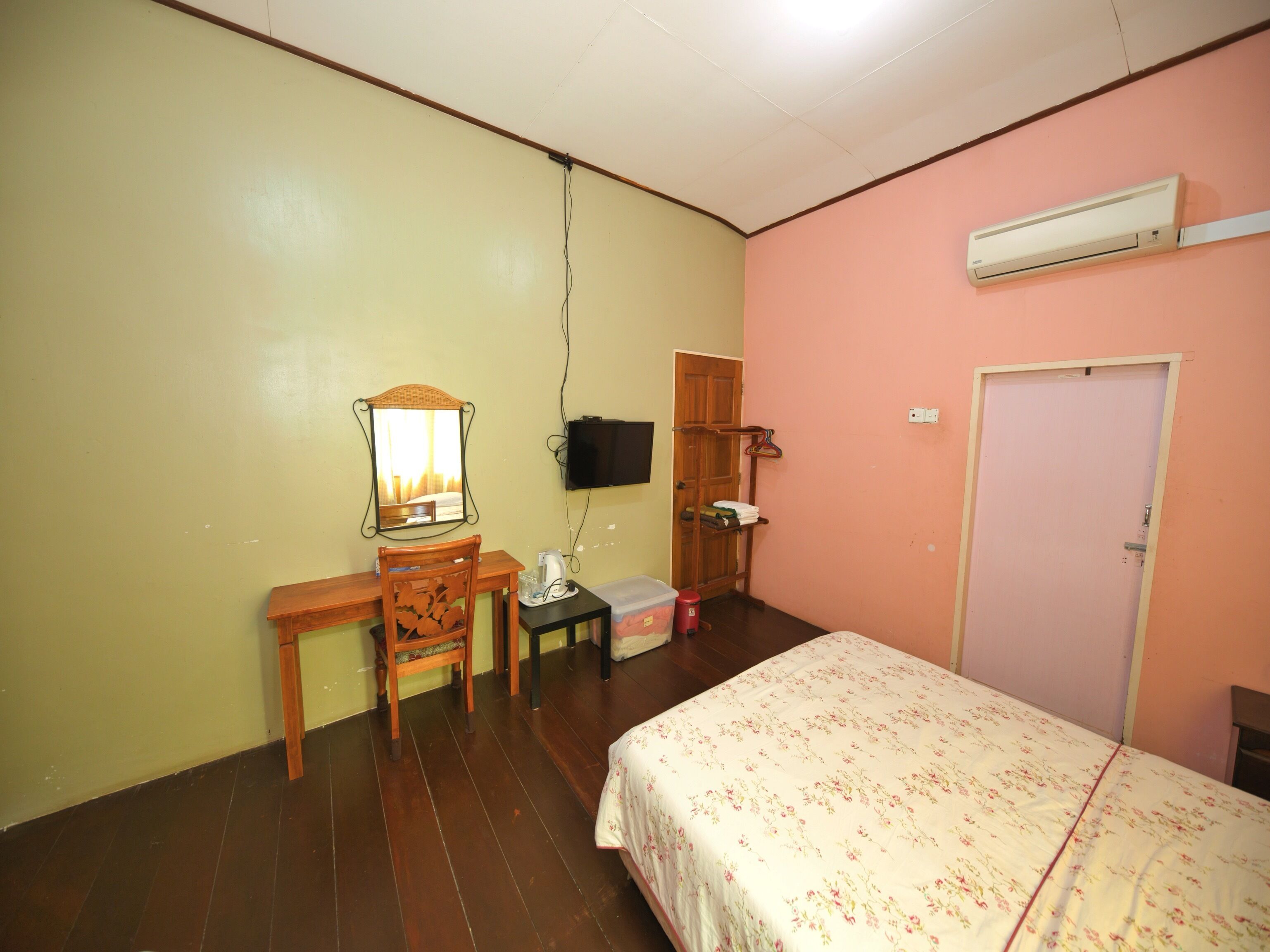 A bedroom with a bed, a desk with a chair, a television, and an air conditioning unit.