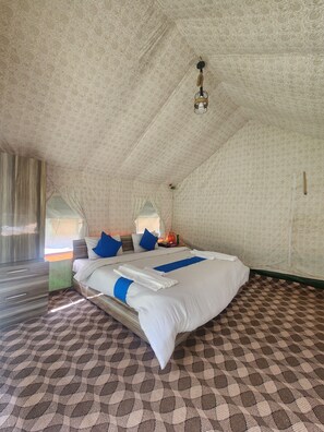 A bedroom with a patterned floor, a bed with white bedding and blue accents, a wooden wardrobe, and a ceiling light fixture. - Snowber Resorts (Gund)