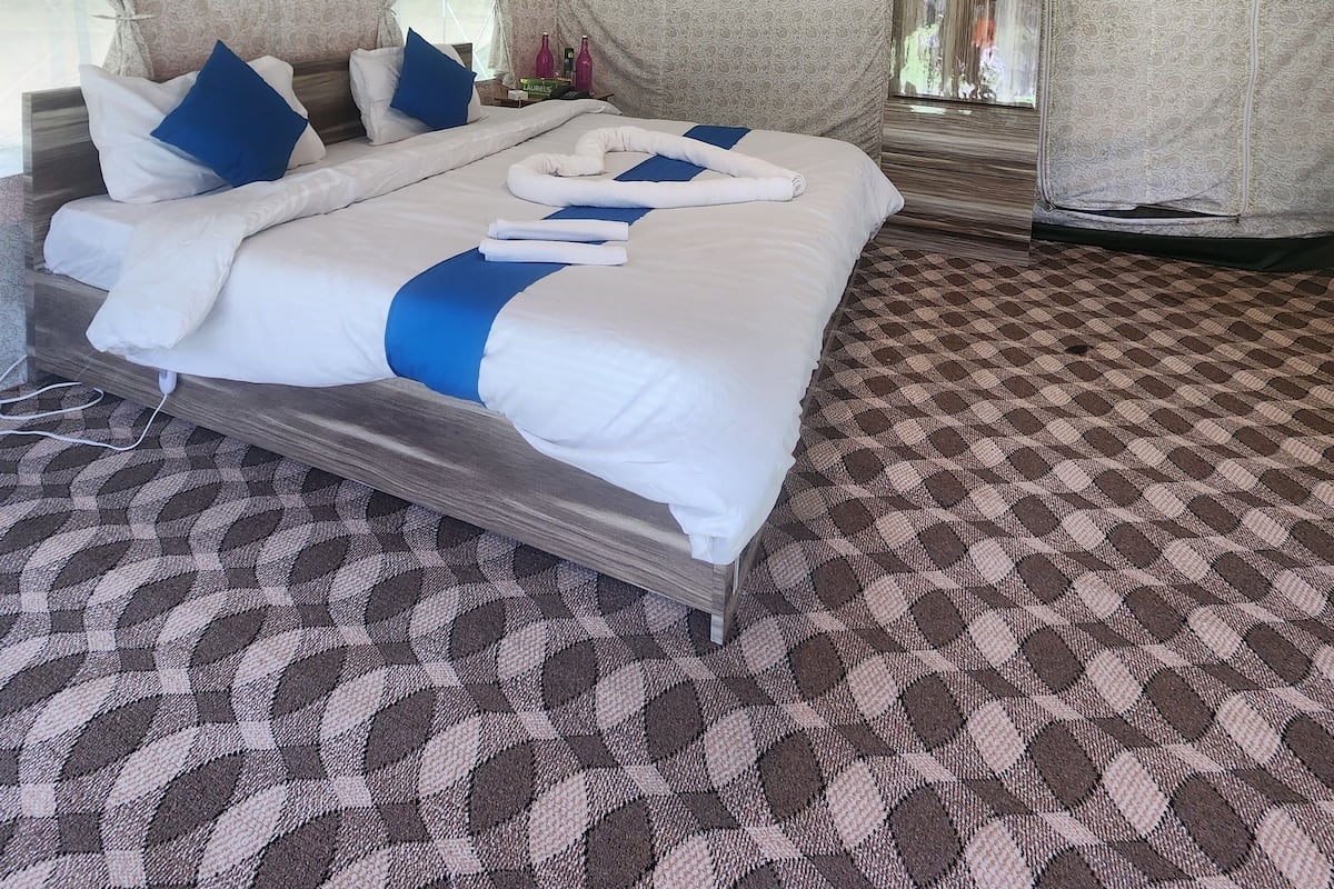 Um quarto em estilo tenda espaçoso e bem iluminado, com uma cama grande, carpete estampado e uma janela com cortinas.