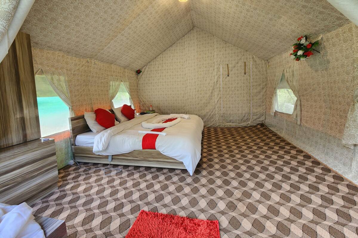 Um quarto tipo tenda com uma cama, uma mesinha e uma janela.