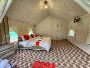 Una habitación tipo tienda de campaña con una cama, una mesita y una ventana.