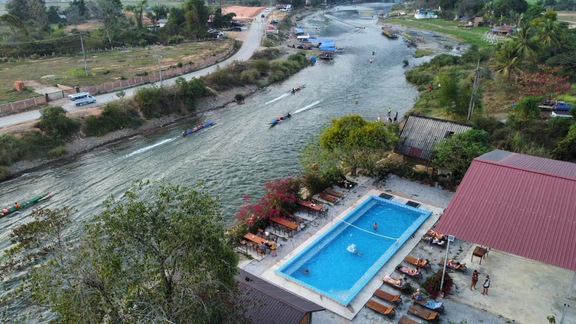A river with boats, a swimming pool, and a red-roofed building.