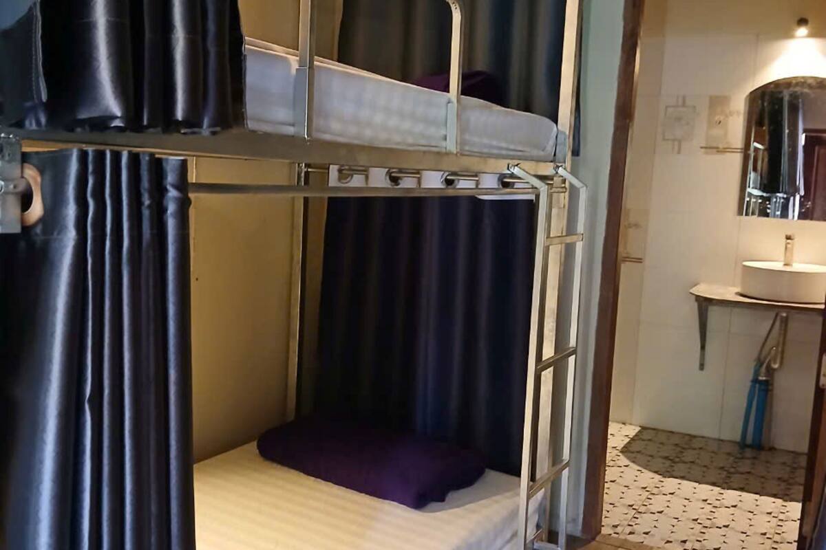 A bunk bed room with a wooden floor, a bathroom with a sink and mirror, and a curtain.