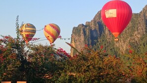Three hot air balloons in a natural setting with a mountainous backdrop. - Riverside Garden Hostel (Vang Vieng)
