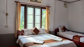 A hotel room with two beds, a large window with curtains, an air conditioning unit, and a small fan on the wall. - Riverside Garden Hostel (Vang Vieng)