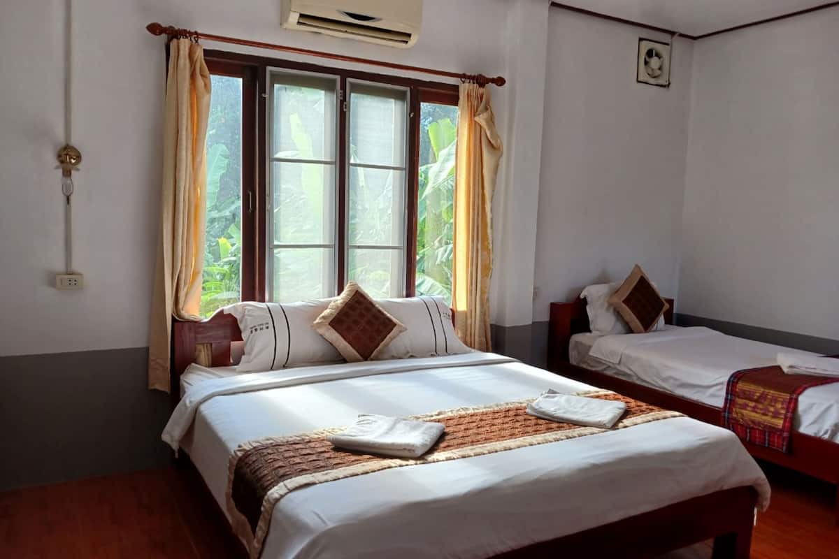 A hotel room with two beds, a large window with curtains, an air conditioning unit, and a small fan on the wall.