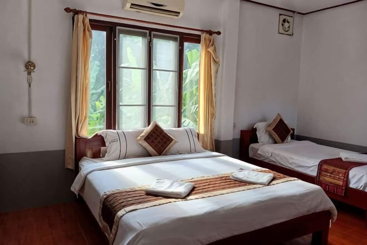 A room with two beds, a window with curtains, a wall clock, and a bed with a blanket.