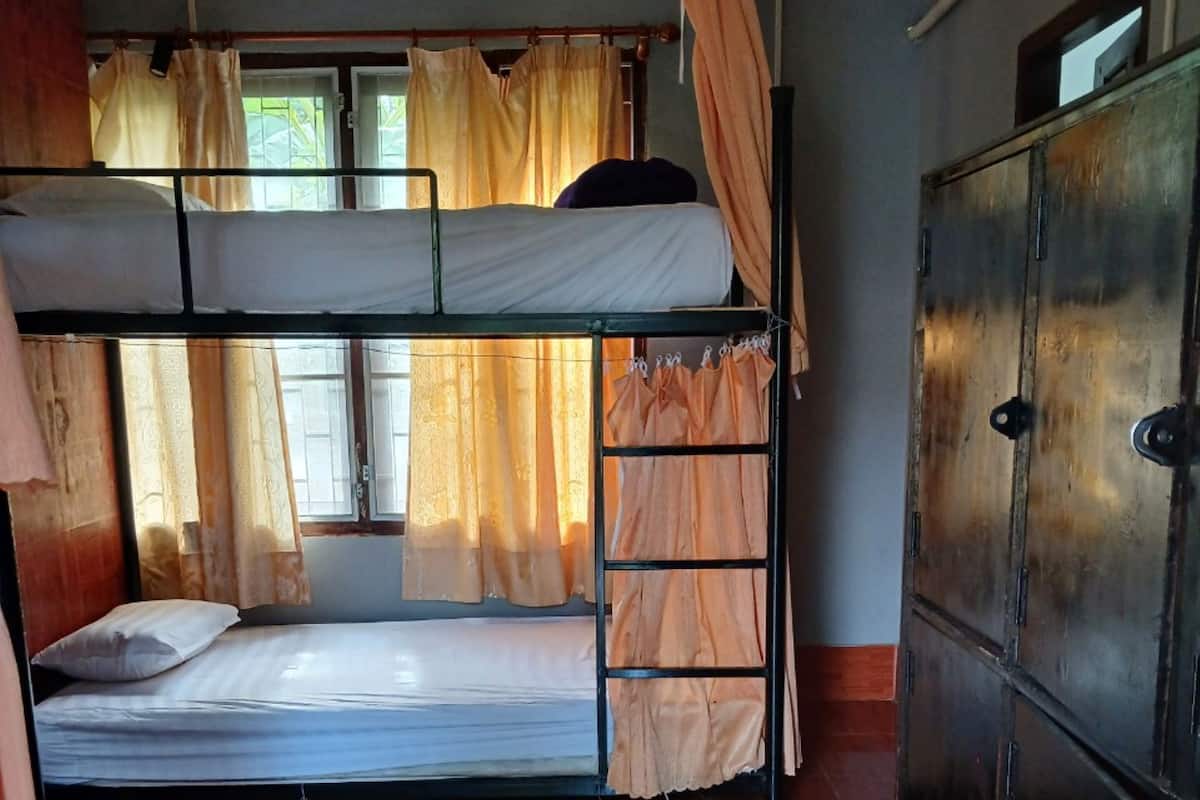 A bunk bed room with a wooden floor, a wardrobe, and curtains on the windows.