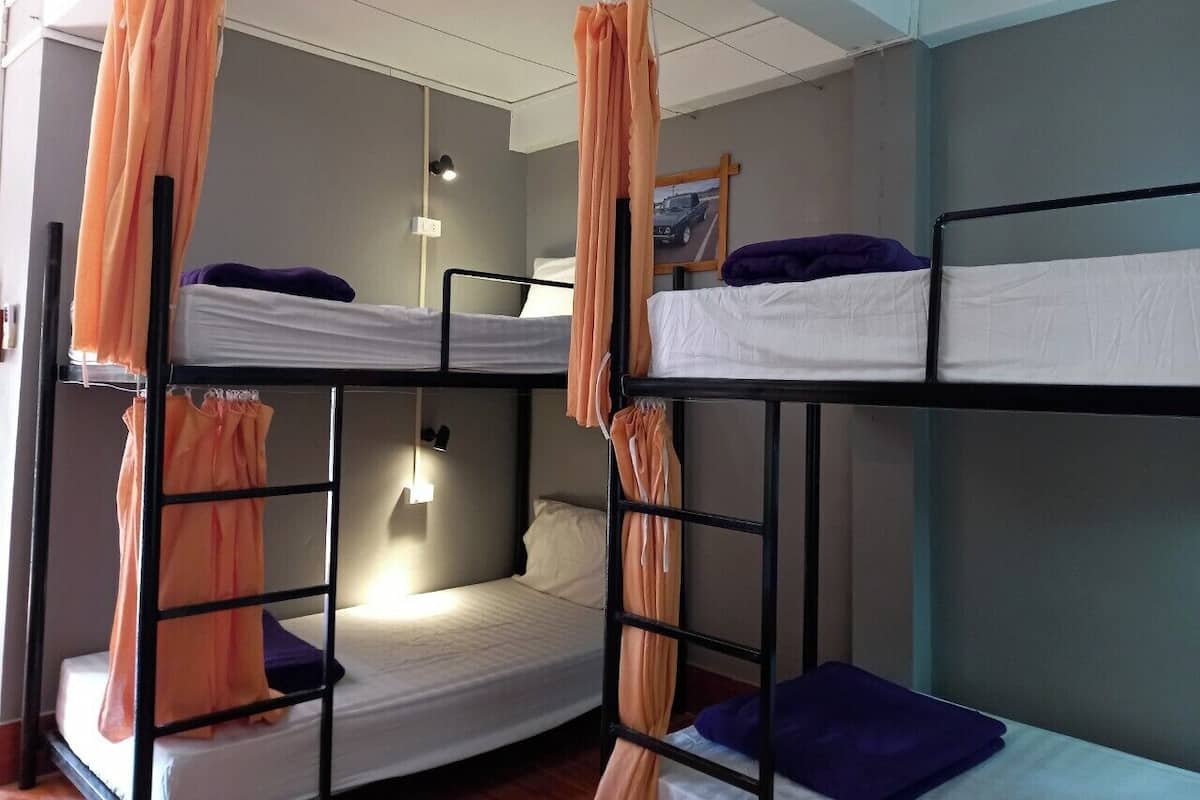 A dormitory room with bunk beds, a bedside table, and a wall-mounted light.