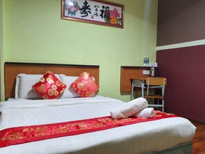 Habitación de hotel con cama, almohadas, un paño decorativo rojo, cabecera de madera, escritorio con una silla y un cuadro en la pared.