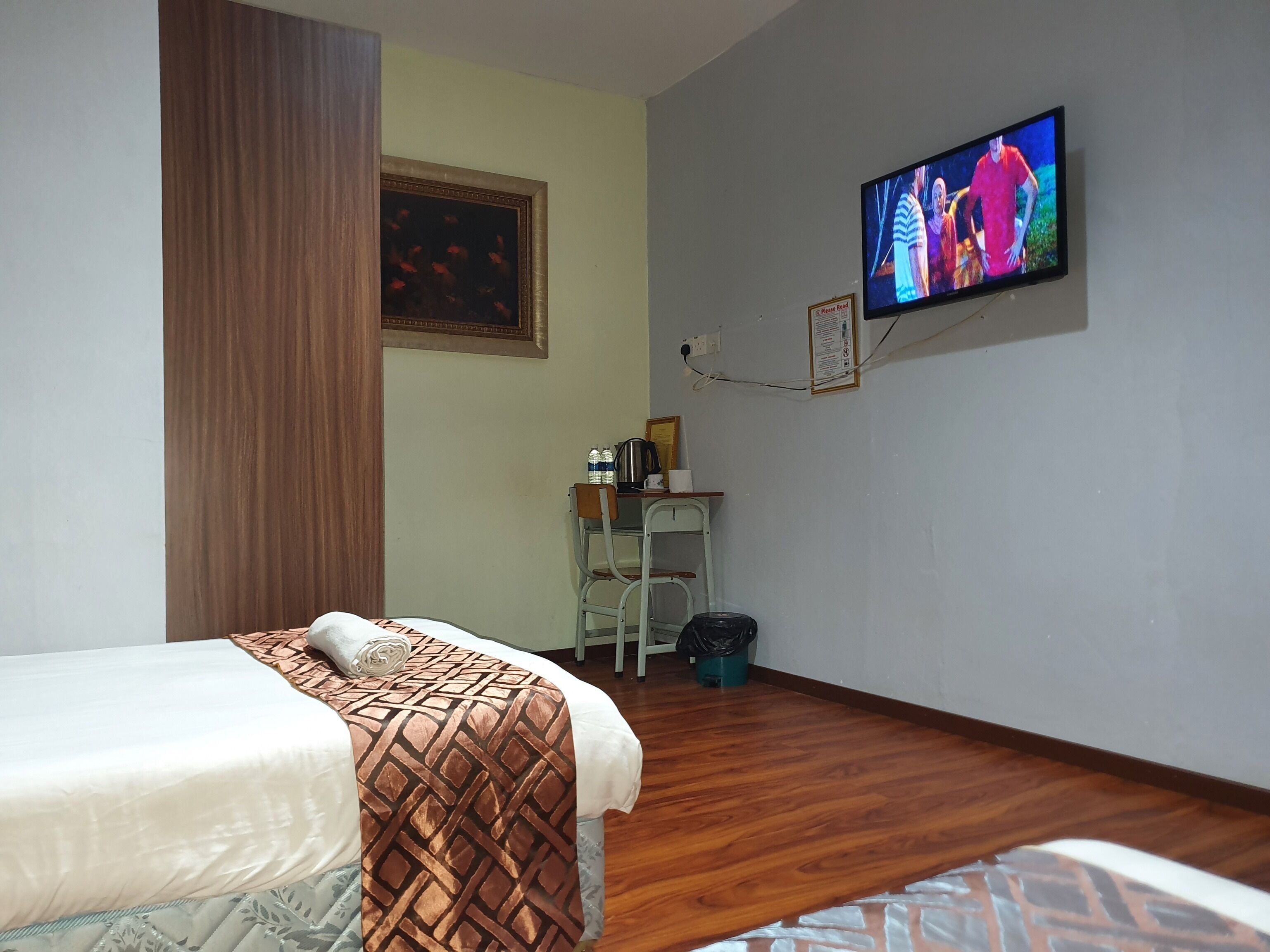 A hotel room with a bed, a desk with a chair, a television, and a painting on the wall.