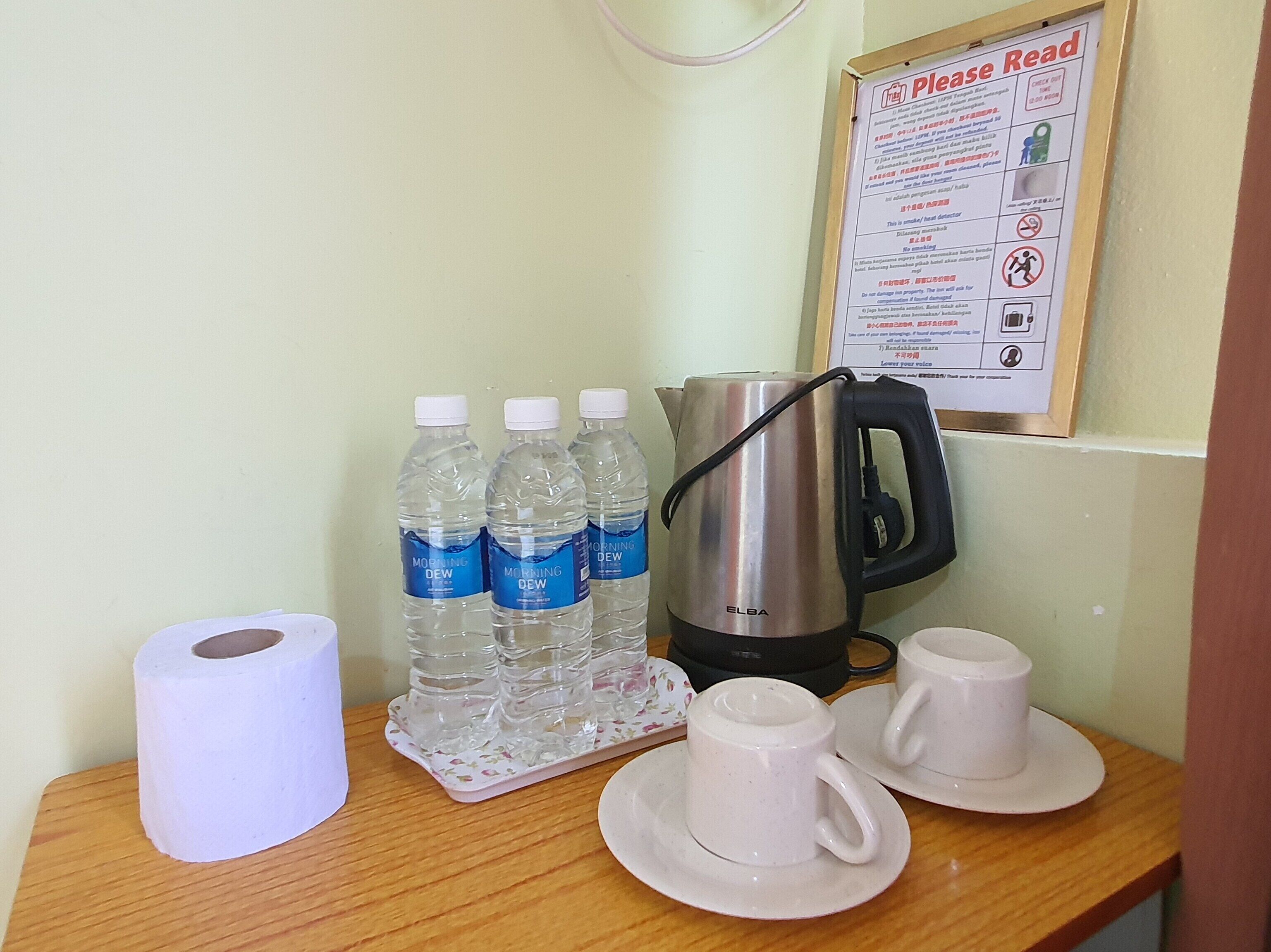 A table with a kettle, water bottles, a roll of toilet paper, and two cups on saucers.
