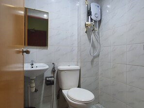 Un baño con inodoro, lavabo y cabezal de ducha manual fijado a la pared.