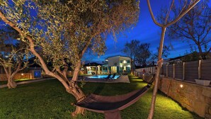 A backyard with a hammock, a swimming pool, and a house with a stone wall.