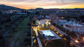 A modern house with a swimming pool, surrounded by a well-maintained lawn and a view of distant hills.